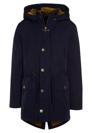 Parka marine imperméable avec capuche doublée en fausse fourrure, fermeture à zip et taille ajustable par cordon. Présente des boutons dorés et deux poches avant.