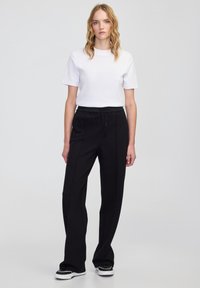 Czarne dopasowane spodnie z elastycznym paskiem w talii, zestawione z gładką białą koszulką z krótkim rękawem. Gładki materiał, prosty krój nogawki.