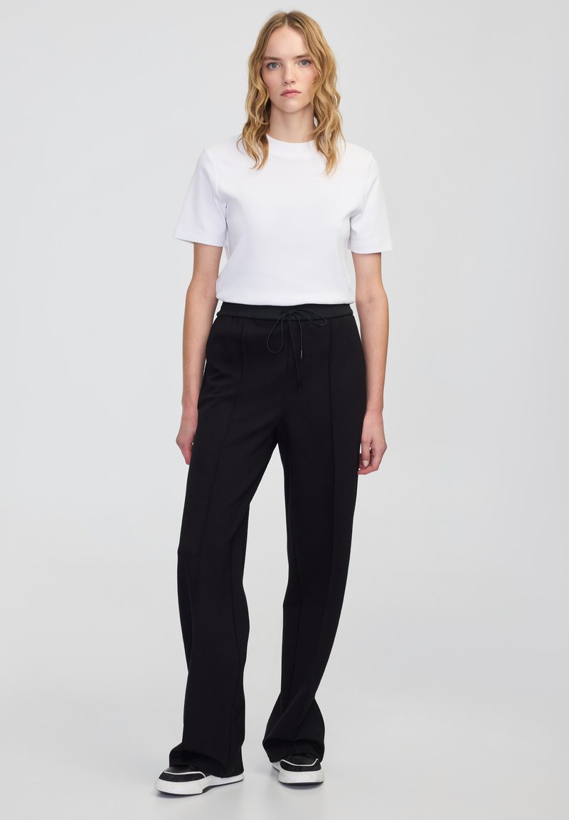 Czarne dopasowane spodnie z elastycznym paskiem w talii, zestawione z gładką białą koszulką z krótkim rękawem. Gładki materiał, prosty krój nogawki.