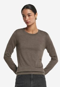 Brązowy, długi sweter z rękawami w dopasowanym fasonie z okrągłym dekoltem i prążkowanymi mankietami. Wykonany z miękkiego, lekkiego materiału.
