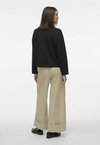 Sort cropped sweatshirt med lange ærmer, parret med beigefarvede vidde bukser med opsmøg og sorte flade sko, set bagfra.