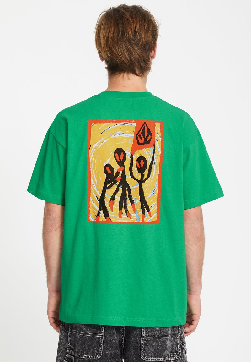 T-shirt en coton vert avec un graphisme coloré au dos, présentant des figures abstraites, sur un fond jaune en spirale, dans une bordure orange.