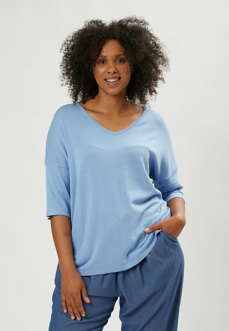 Top azzurro chiaro con scollo a V e maniche corte, realizzato in un tessuto morbido. Indossato con pantaloni larghi azzurro chiaro. Texture liscia e vestibilità casual.