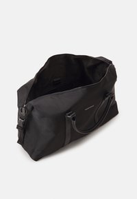 Μαύρη νάιλον τσάντα duffle με δερμάτινες λαβές, κλείσιμο με φερμουάρ και εσωτερικές θήκες. Διαθέτει διακριτό λογότυπο και λεία υφή.