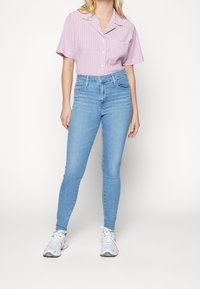 Ljusblå smala jeans som kombineras med en kortärmad, röd och vit rutad skjorta. Sneakers med vita snörningar fulländar outfiten.