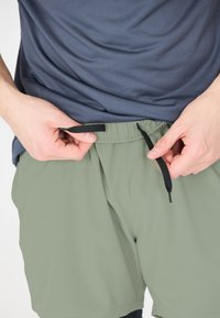 Herrshorts med elastisk midja i mjukt, ljusgrönt tyg. Svarta snoddar i midjan för justerbarhet. Slät textur, avslappnad design.