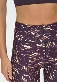 Leggings w kolorze purpurowym z brązowym i kremowym wzorem zwierzęcym. Wysoki stan, dopasowany krój i detal w postaci bocznej kieszeni. Miękka, elastyczna tkanina.