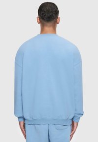 Lys blå sweatshirt med en afslappet pasform, ribbede manchetter og kant, samt en glat tekstur. Synlig syning langs skuldersømmene.