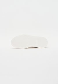 Semelle de sneaker blanche avec une surface en caoutchouc texturé, présentant un motif de semelle géométrique et une empreinte de logo près du talon.