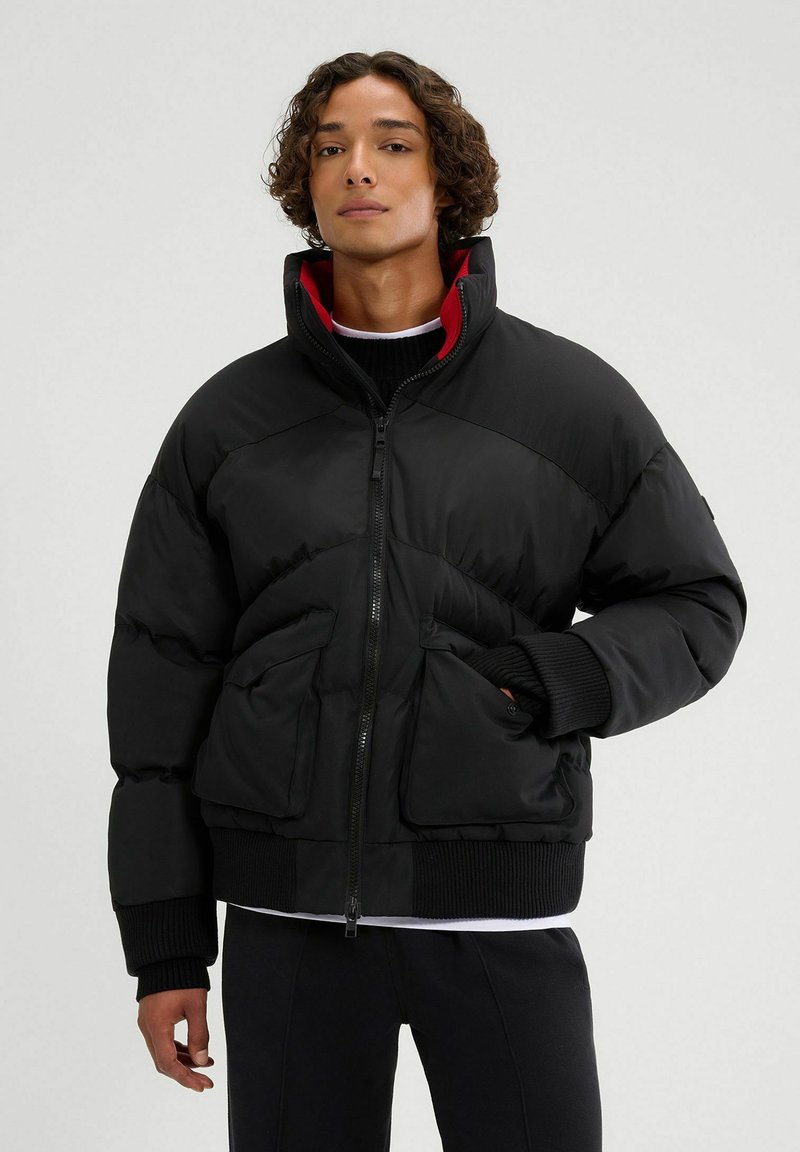 Czarna kurtka puchowa z wysokim kołnierzem, z zamkiem z przodu i ściągaczami u mankietów. Posiada czerwoną podszewkę oraz dwie przednie kieszenie w prostokątnym kształcie.