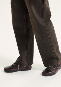 Zapatos de lona negros con acentos rojos y cordones redondos, combinados con pantalones de mezclilla oscuros de corte holgado y dobladillos deshilachados.