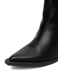 Czarne skórzane botki za kostkę z ostrym noskiem, teksturowaną powierzchnią i eleganckim wzornictwem. Posiadają płaską, cienką podeszwę i minimalne przeszycia.