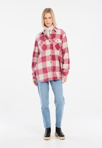 Chemise en flanelle à motif à carreaux rose et crème, avec deux poches poitrine et fermeture par boutons. Associée à un jean bleu clair et des bottes à plateforme noires.