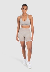 Jasnobeżowy sportowy stanik i pasujące, wysokie szorty, dopasowany krój, miękka fakturowana tkanina, subtelny wzór, cienkie ramiączka. Białe trampki.