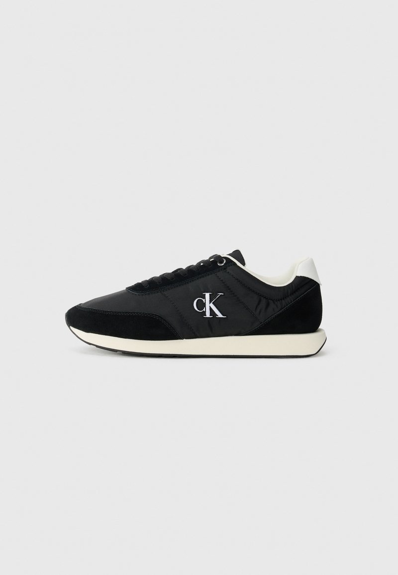 Zwarte sneaker van nylon en suede, met een wit logo, contrasterende zool en ronde neusdesign met veters. Gladde en gestructureerde oppervlakken.