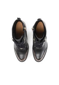 Par de botas negras de cuero hasta el tobillo con borde marrón texturizado, cordones negros, cremallera lateral y ojales de metal, vistas desde arriba.