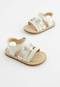 Weiße Sandalen mit mehreren Riemen, einer gepolsterten Innensohle und einem dekorativen silbernen, glitzernden Herzdetail. Gummisohle für besseren Halt.