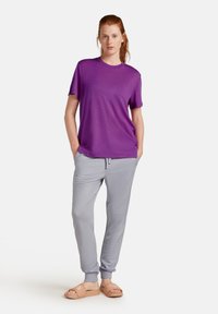 Camiseta de manga corta morada y pantalones jogger gris claro con puños elásticos y bolsillos, combinados con sandalias tipo slide beige.