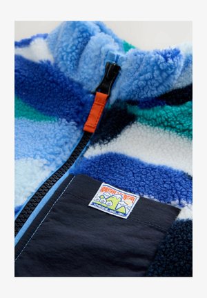Flisasta jakna z abstraktnim vzorcem v modri, zeleni in beli barvi. Ima črn žep, oranžno zadrgo in znamko na aplikaciji. Mehka tekstura.