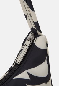 Svart och krämfärgad mönstrad väska med en slät yta; har en dragkedjestängning, kort handtag och en strukturerad form.