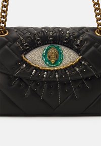 Czarna pikowana skórzana torba z złotymi łańcuszkami, z haftowanym i koralikowym wzorem oka oraz złotym ozdobnym środkiem.