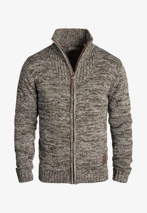 Brown and cream knitted sweater with a high collar, full zipper, ribbed cuffs, and a textured pattern. Features a small logo patch at the hem.