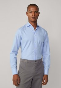 Lichtblauw, langgerek shirt met lange mouwen en een button-down kraag, met een subtiel textuurpatroon; gecombineerd met grijze chino's.