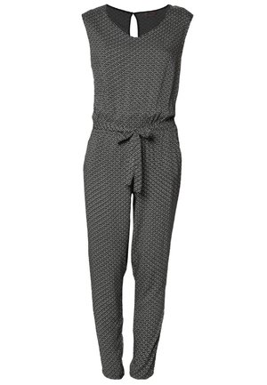 Woman wearing patterned black and white jumpsuit with a tied waist, black blazer, black heels, and holding a black clutch.