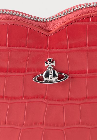 Επιφάνεια από κόκκινο δερμάτινο υλικό με ασημένιο φερμουάρ στην κορυφή και ένα λαμπερό ασημί σφαιρικό και σταυρό έμβλημα τοποθετημένο στο κέντρο κάτω από το φερμουάρ.