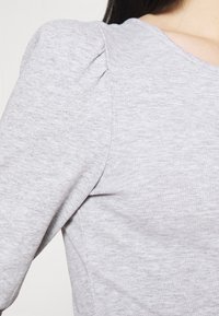 Light gray ribbed top featuring puffed shoulder detailing, with a rounded neckline and textured fabric, emphasizing softness and comfort.
