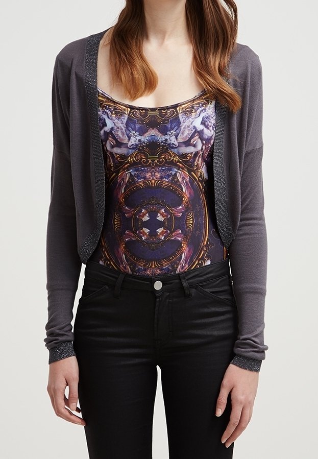 Grå cardigan med glittrig kant, lager på lager över en flerfärgad mönstrad topp. Svarta slim fitjeans fulländar outfiten.