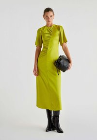 Abito verde lime con maniche corte a sbuffo e ruching diagonale. Abbinato a una borsa nera rotonda e stivali neri al ginocchio.