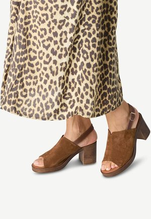 Brune ruskinds åben-tå slingback sko med en stablet hæl og justerbar rem. Båret med en leopardprint nederdel. Teksturdetaljer på hælen.
