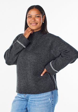 Pilkas megztinis su aukštu kaklu, su baltomis siūlėmis ant rankovių ir laisvo kirpimo. Sujungta su šviesiai mėlynomis džinsomis.