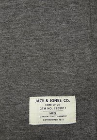 Etichetta di abbigliamento su tessuto grigio con testo: "JACK & JONES CO. CORP. DI DK CTM N. 7203011 MFG. ABBIGLIAMENTO PRODOTTO FONDATA NEL 1975."