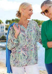 Bunt gemustertes Hemd mit knöpfigem Ausschnitt, leichtes Material, lange Ärmel, kombiniert mit einem blauen Pullover und weißen Hosen.