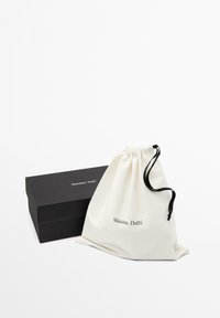 Sort rektangulær Massimo Dutti-boks ved siden af en hvid snørepose med sorte snore og brandnavn trykt på begge.