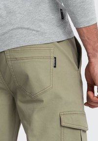 Cargo kalhoty z jemné olivově zelené bavlněné twill látky s vyztuženým švem, šikmými kapsami a malou černou značkovou štítkem.