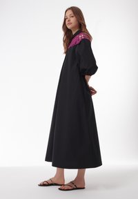 Robe longue noire avec des manches bouffantes et un col en dentelle magenta décoratif. Assortie à des sandales noires à lanières avec des accents métalliques.