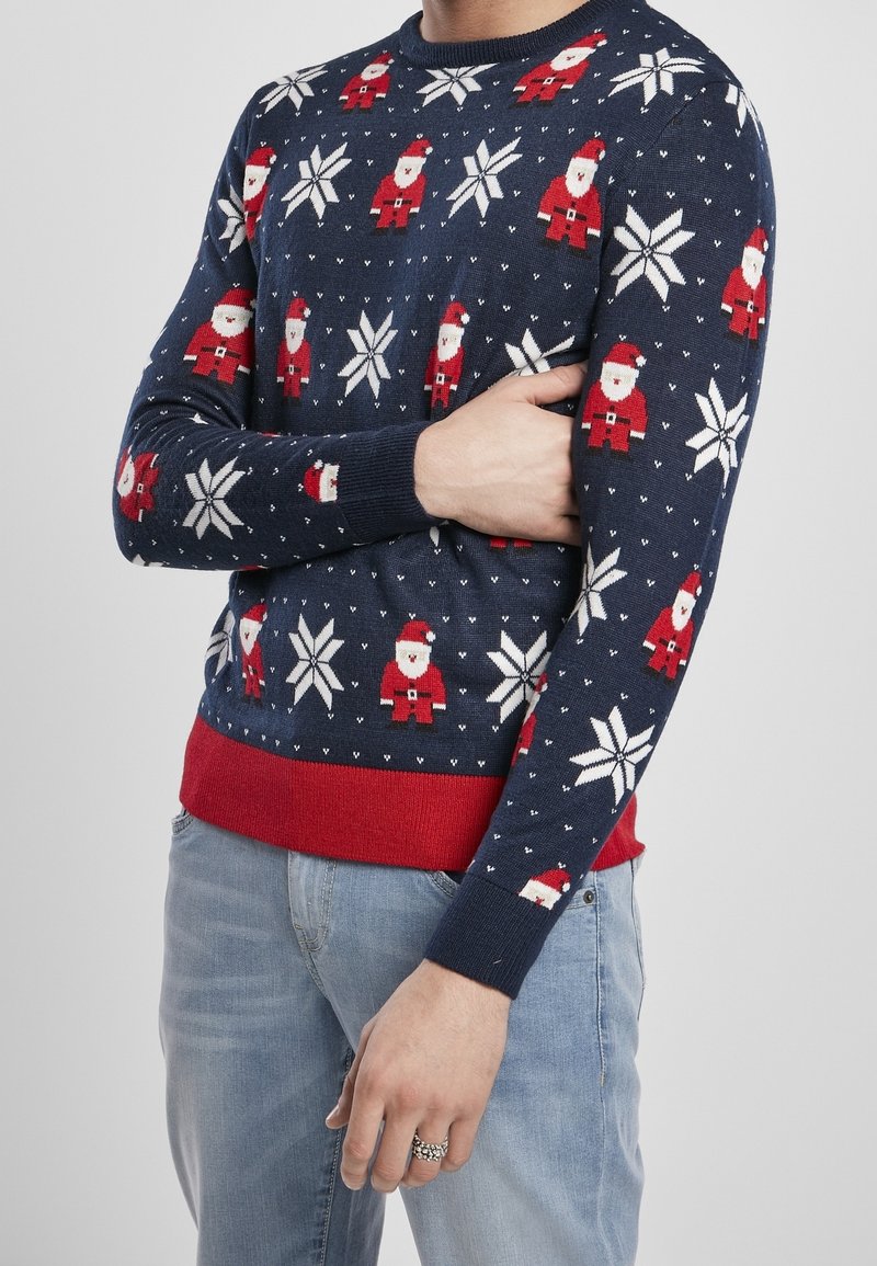 Pull festif bleu marine avec des motifs de Santa et de flocons de neige. Il dispose d'un ourlet et de poignets côtelés rouges, fabriqué en matériau doux tricoté.