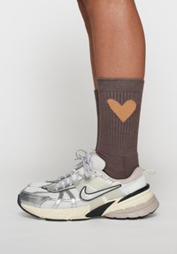 Calzino grigio a coste con design a cuore arancione, abbinato a una scarpa sportiva bianca e argento con dettagli e lacci neri.