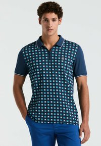 Polo shirt bleu marine avec un motif géométrique de carrés bleus, à manches courtes et col classique. Présente un petit logo sur la poitrine gauche.