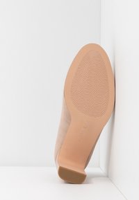 Chaussure à talon haut en daim beige avec un bout arrondi, une semelle beige lisse dotée d'un motif antidérapant texturé, et un talon bloc bas.