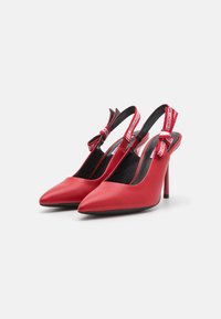 Raudoni odiniai slingback kulniukai su smailiu priekiu, aukštu stileto kulnu ir dekoratyviu dirželiu, kuriame yra kontrastingas tekstas gale.