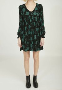 Vestido negro con flores que presentan tonos azul verdoso, escote en forma de V, mangas largas abullonadas con puños elásticos y falda acampanada. Combinado con botas negras hasta el tobillo.