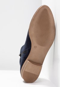 Semelle d'une bottine en daim bleu marine avec fermeture éclair, bout pointu, taille 37 et semelle extérieure en caoutchouc beige légèrement texturée.