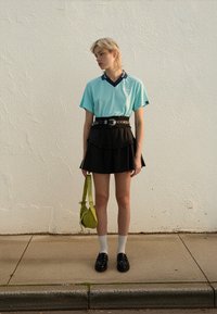 Hele sinine lühikeste varrukatega pluus tumesinise kraega, kihiline must volditud seelik, mustad kingad, valged sokid ja roheline risti kandmisega kott.