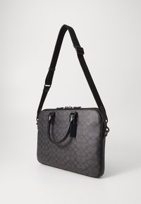 Black laptop bag made of textured material, featuring a geometric pattern, dual top handles, and a detachable shoulder strap. Zipper closure.