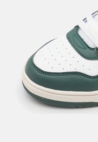 Białe sneakersy z zielonym skórzanym czubkiem, perforowanym wzorem i teksturowanym wykończeniem. Posiadają białe sznurowadła i kremową podeszwę.