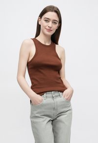 Brązowy prążkowany top na ramiączkach z okrągłym dekoltem, zestawiony z jasnoszarymi dżinsami. Tkanina wydaje się gładka, dopasowana i ma swobodny design.